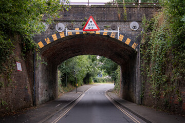 Low brick railway bridge over narrow road with height restriction sign