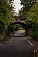 Low bridge warning sign over empty road passing under a railway bridge