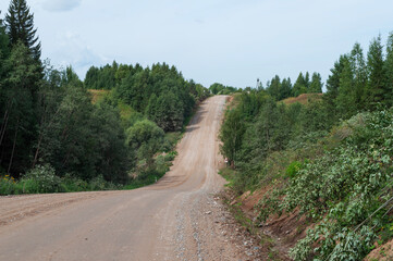 Country dirt road through forested hills, steep climbs and descents, clear summer day