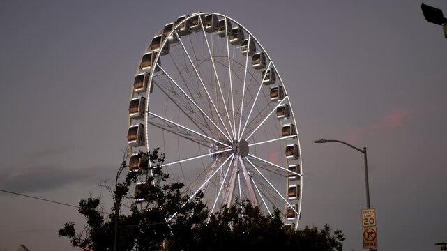Slow motion landscape of Ferris wheel carnival ride nighttime illuminated lights attraction pier city CBD of San Francisco Embarcadero waterfront USA America California bay area