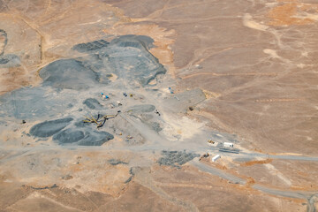 An open pit mine or quarry with machinery, excavators, bulldozers, and trucks digging and extracting black rock coal, charcoal or smut in the middle of the Sahara desert arid land reg. 