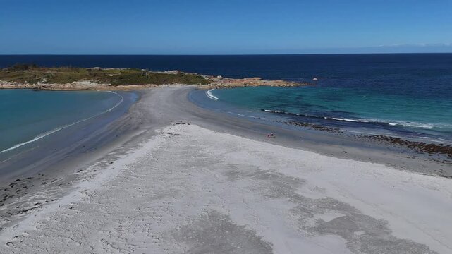 Walking people along sandy beach of Bicheno City in Tasmania. Visiting Diamond Island during sunny day with blue sky. Aerial orbit shot.