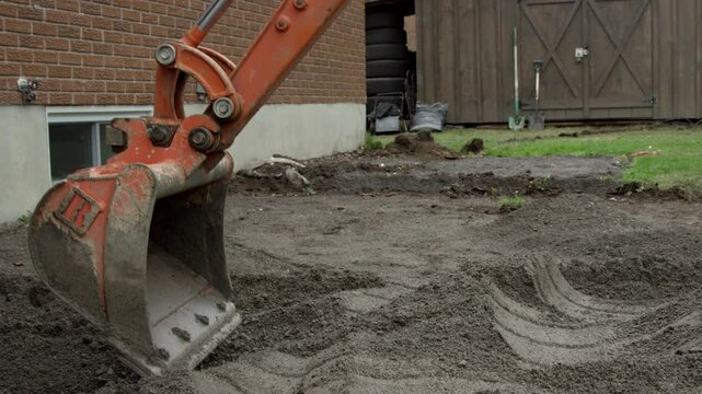 Mini excavator digging foundation for repairs on residential house - side profile of excavtor bucket scraping