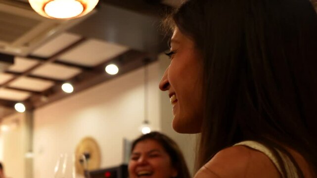 Hispanic woman clinking glass of wine with friends in restaurant. Closeup shot