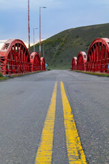 vertical view of a road heading towards the pass of a red bridge and mountains of green and desert vegetation, street guided by two lines of yellow road