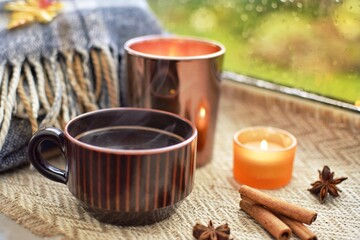 Warm cozy composition on the window. It's raining outside, warm tea with cinnamon and candles on the windowsill. Autumn concept.