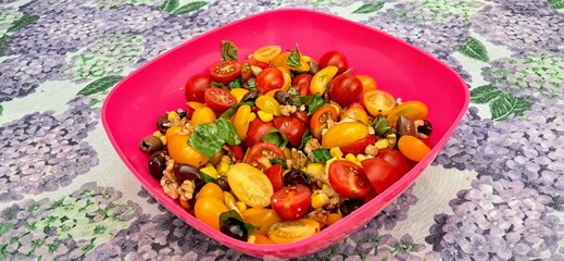 Mixed salad vegetables consisting of a red and yellow tomatoes, basil parsley walnuts corn celery. Fresh summer vegetables to eat as a side dish or as a main course. Table with purple floral tableclot