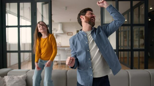 Positive Caucasian child little girl jumping couch man male parent carefree family dancing to music dad daughter fooling around. Kid father smiling laugh sing having fun together at home happy leisure