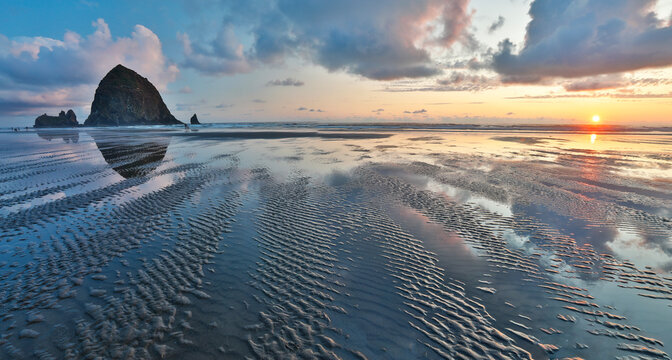 USA, Oregon, Cannon Beach. Sunset golden colors with ripples in sandy beach and The Haystack Rock