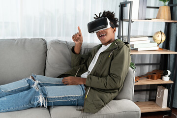 Surprised African American looking VR enjoy watching leaning back sofa by touching air in fantastic 3D cartoon movie technology virtual reality metaverse journey new world at living room. Contrivance.