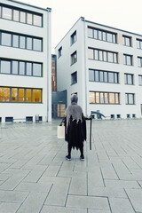 Back view of kid in grim reaper Halloween costume with scythe and bag for sweets at school building...