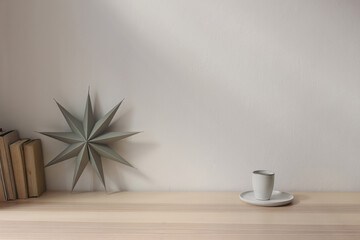 Winter decorated interior, living room. Grey folded paper star, cup of coffee and books on wooden table background. Christmas decoration, festive breakfast. Scandinavian design. White wall mockup.