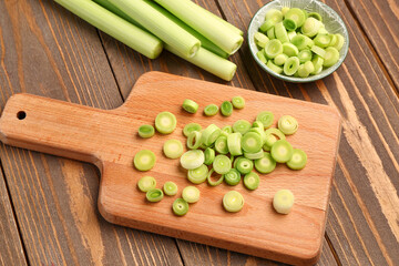 Board and bowl with slices of fresh leek on wooden background