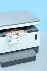 Laser printer with euro banknotes on table near blue wall