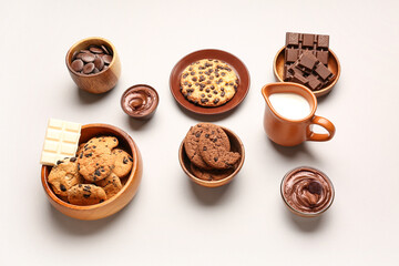 Bowls with cookies, chocolate and jug of milk on white background
