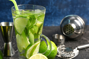 Glass of cold mojito and shaker with lime on black table
