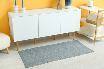 Stylish interior of living room with drawers, bench, shelving unit and soft rug