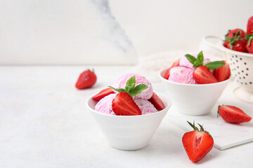 Bowls of strawberry ice cream with berries and mint on white table near grunge wall