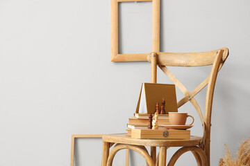 Books with chess pieces and cup of coffee on chair in light room