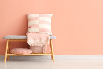 Grey bench with cushions and blanket near pink wall