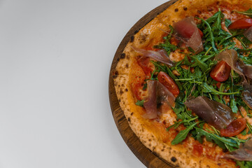 Pepperoni pizza with arugula and prosciutto. Meat pizza with cheese, cherry tomatoes and fresh arugula on a white background