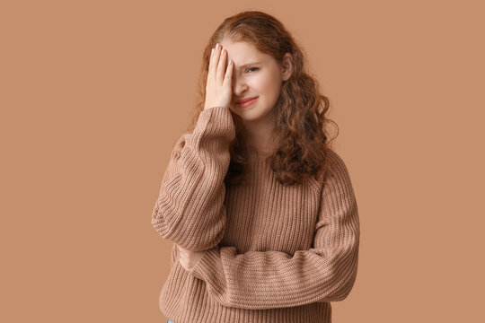 Portrait of ashamed young woman covering face on brown background