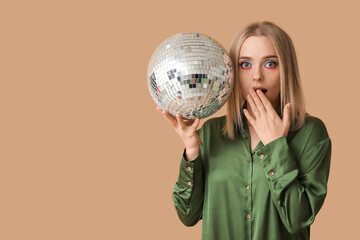 Beautiful shocked young woman with disco ball on brown background