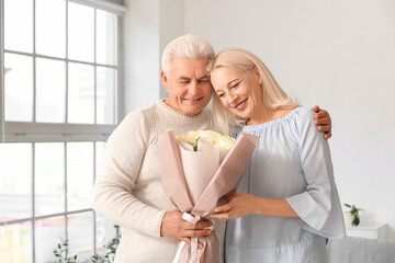 Mature man giving his wife bouquet of roses at home