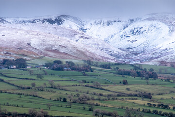 Obraz premium Snow covered mountains with green fields below in a wintery landscape