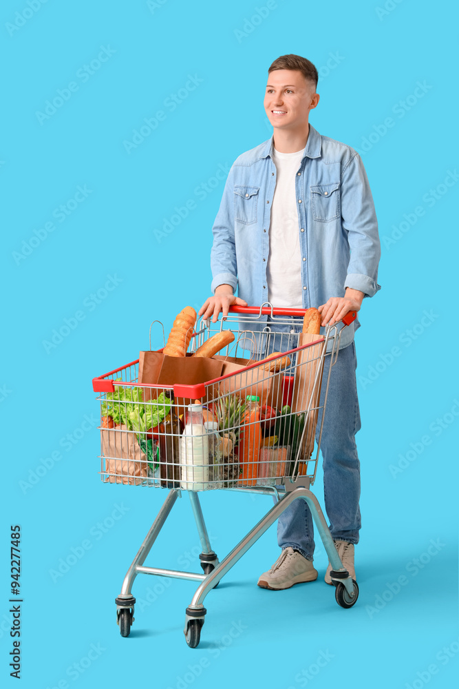 Wall mural young man with full shopping cart on blue background