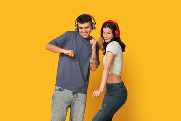 Beautiful young couple in headphones dancing on yellow background