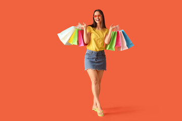 Beautiful young happy woman with shopping bags on orange background. Summer sale concept