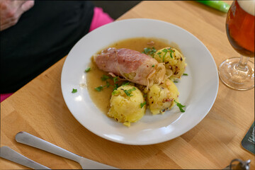 Chicken roll with cabbage and potatoes on a white plate.