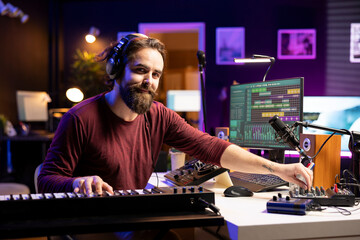 Portrait of male singer playing electronic keyboard notes and adding them on new soundtrack, using...