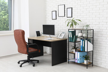 Interior of stylish office with workplace, armchair, modern computer and shelving unit