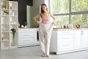 Beautiful young happy woman pointing at loose jeans at home. Weight loss concept