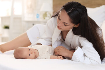 Beautiful young woman in bathrobe with her baby lying on bed at home