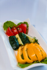 Fresh vegetables tomatoes, yellow pepper and cucumber on a white plate on a white background