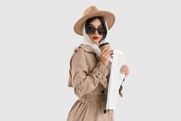 Female spy with newspaper and coffee cup on light background