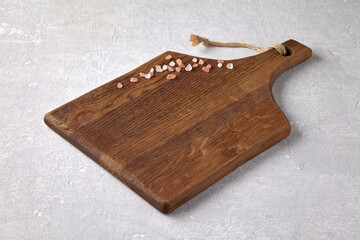 Fototapeta premium white wooden cutting board with scattered coarse pink salt on light stone table for displaying food on menu