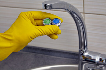 plumber's hand in yellow rubber gloves showing new and old clogged faucet aerator