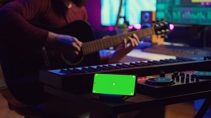 Songwriter playing acoustic guitar in home studio with greenscreen display running on smartphone app. Musician practices singing on musical instrument with strings, isolated screen. Camera A.