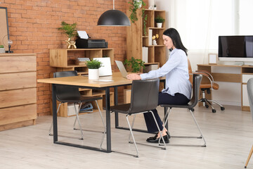 Young woman working with laptop at table in modern office