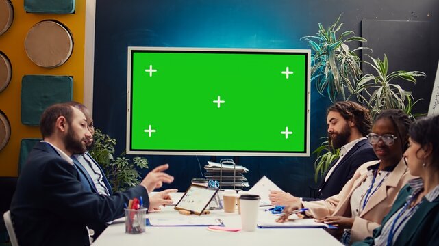 Marketing team meeting in a boardroom with isolated TV display, working together to improve the organization public image and social media presence. Business specialists conduct analysis. Camera B.