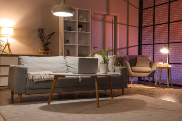 Interior of living room with sofa, armchair, table and glowing lamps