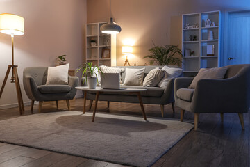 Interior of cozy living room with sofa, table, armchairs and glowing lamps