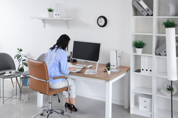 Young woman writing on notebook at workplace with modern computer and laptop in light office