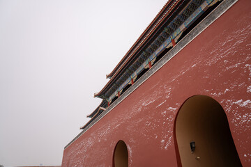 A red wall with arched openings and snow patterns, topped by tiered decorative eaves. The muted...