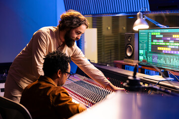 Diverse team of artist and audio engineer composing a hit song, working in professional music studio with technical gear. Musician with expert editing and recording music on mixing console board.