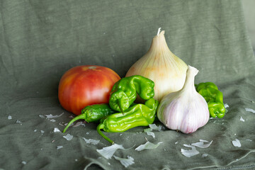Still life of tomato, onion, peppers and garlic on an olive green background.
